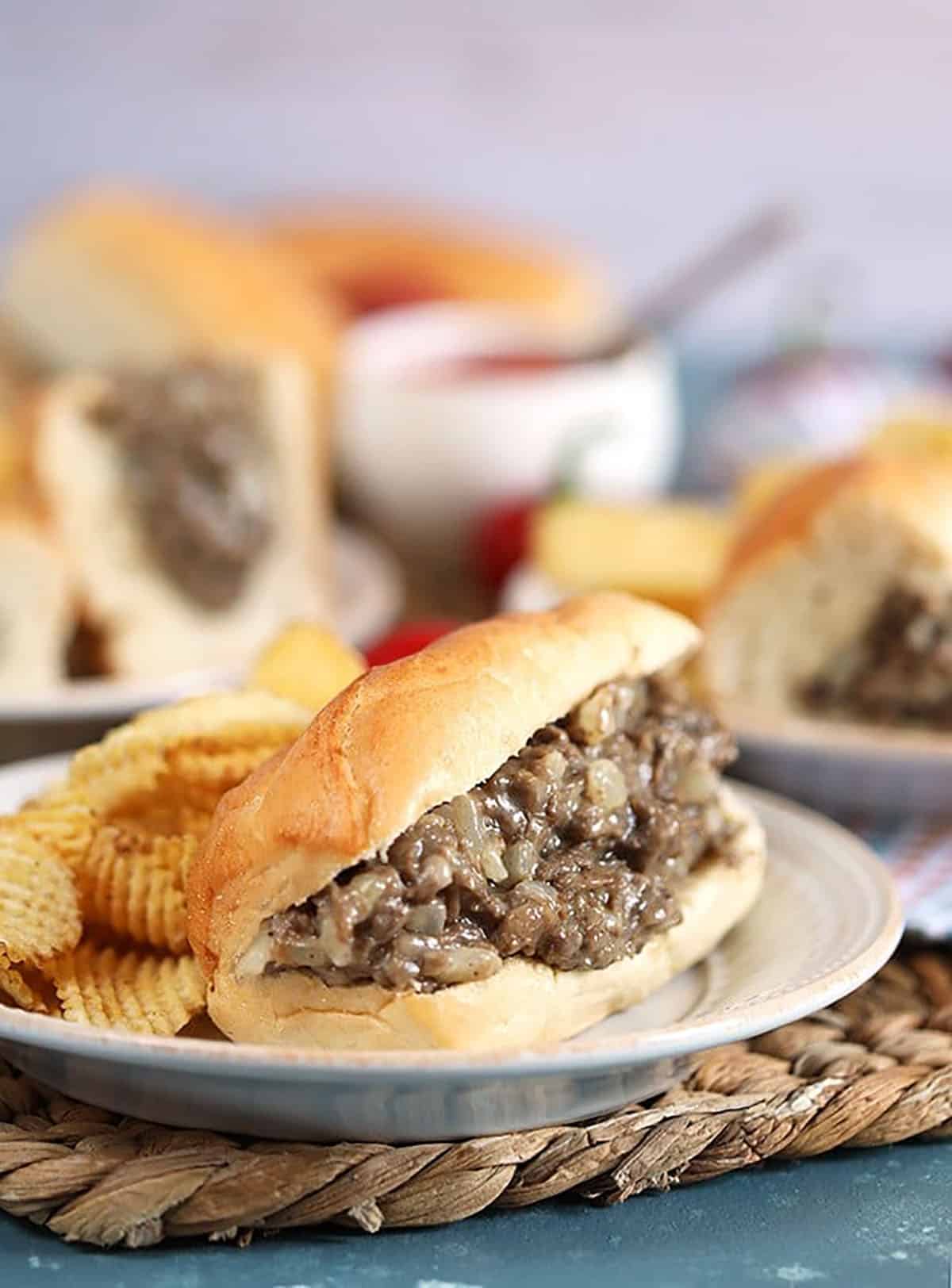 Philly cheesesteak sandwich on a white plate with chips 