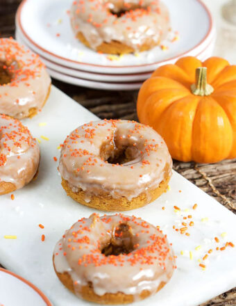 Baked Pumpkin Donuts with glaze on a white board with a mini pumpkin in the background.