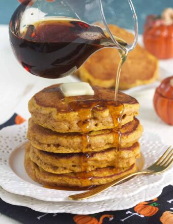 A stack of pumpkin pancakes is being drizzled with syrup.