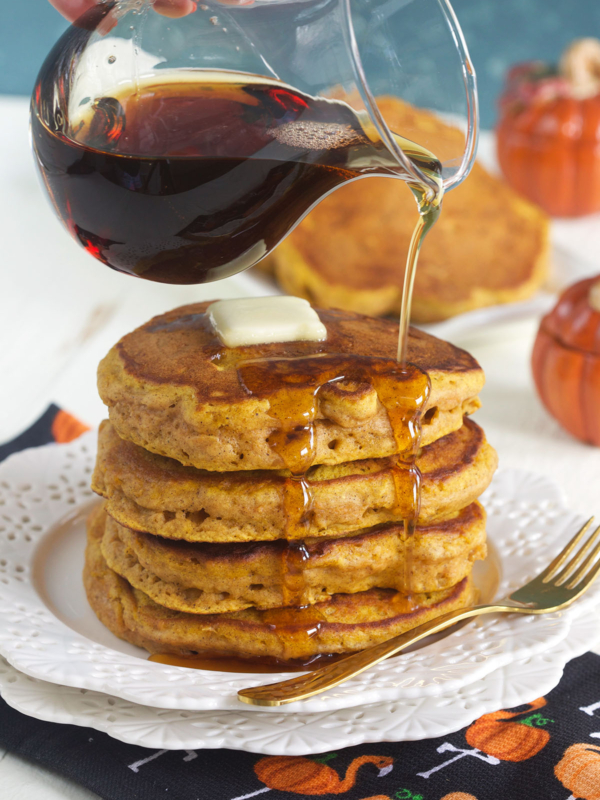 A stack of pumpkin pancakes is being drizzled with syrup.