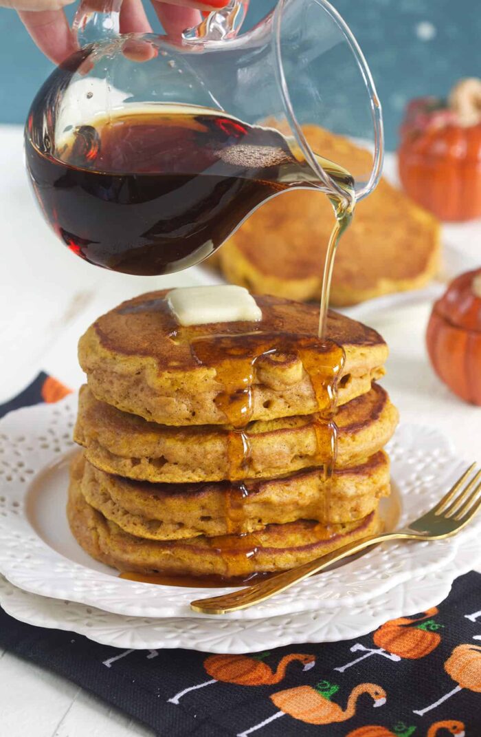 A stack of pumpkin pancakes is being drizzled with syrup.
