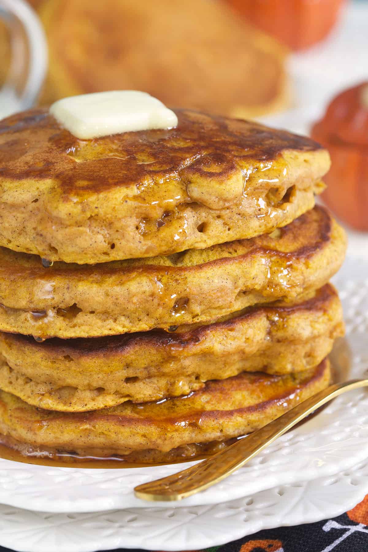 A stack of pumpkin pancakes is topped with butter and syrup.