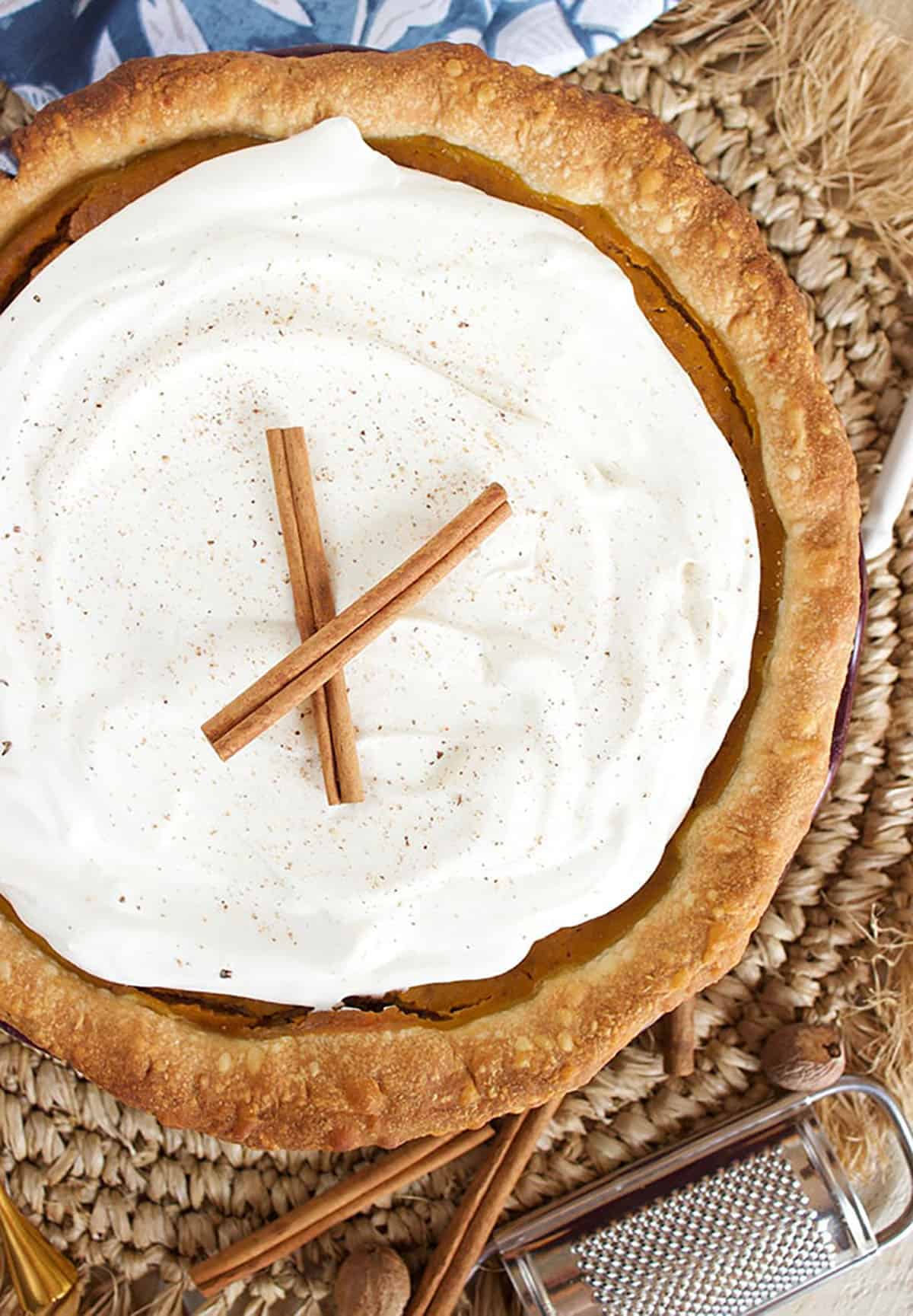 Whole pumpkin pie with whipped cream and two cinnamon sticks on top.