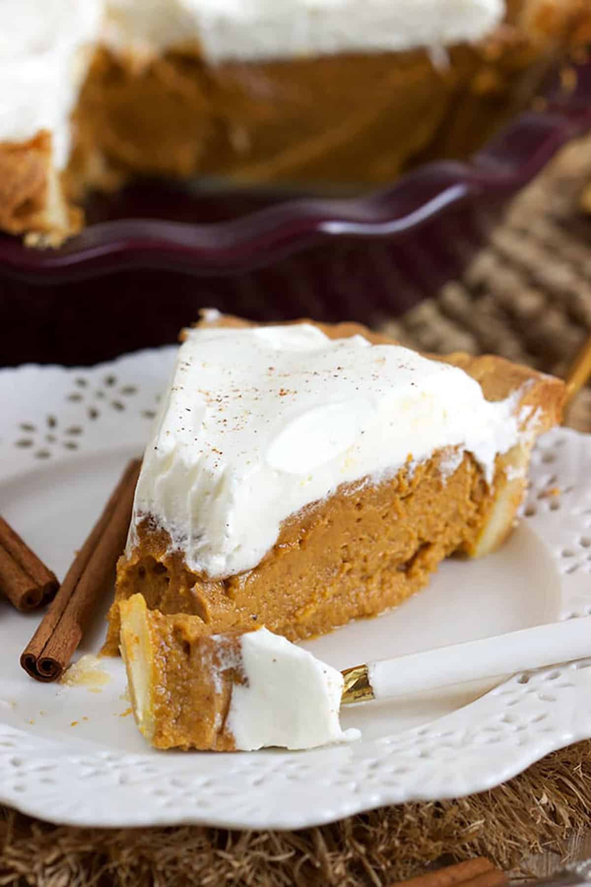 slice of pumpkin pie topped with whipped cream on a white plate with a bite on a fork.