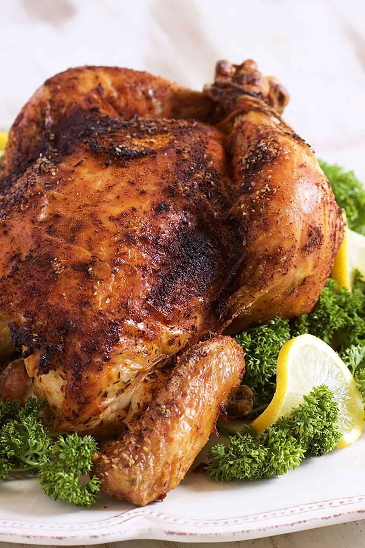 Rotisserie Chicken on a white platter with parsley and lemons.