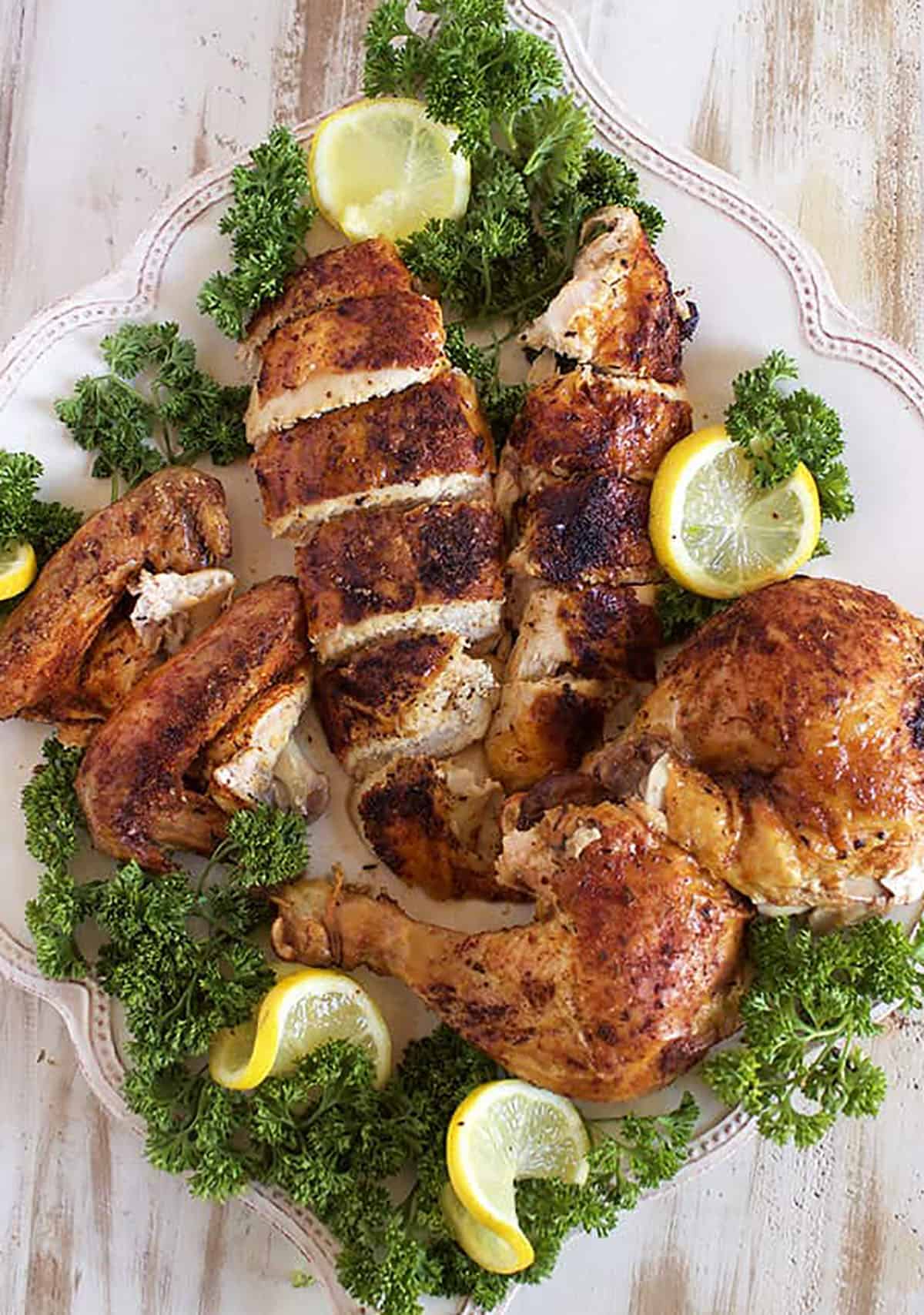Rotisserie Chicken carved and arranged on a square platter with parsley sprigs and sliced lemons.