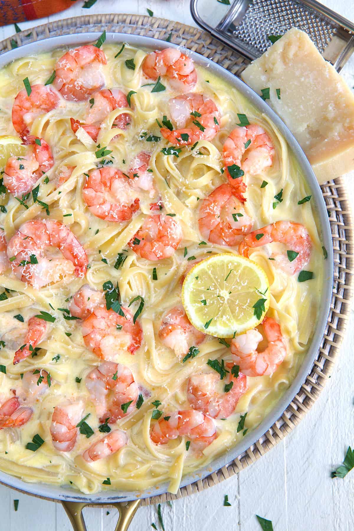 A skillet is filled with shrimp, pasta, sauce, and lemon slices.