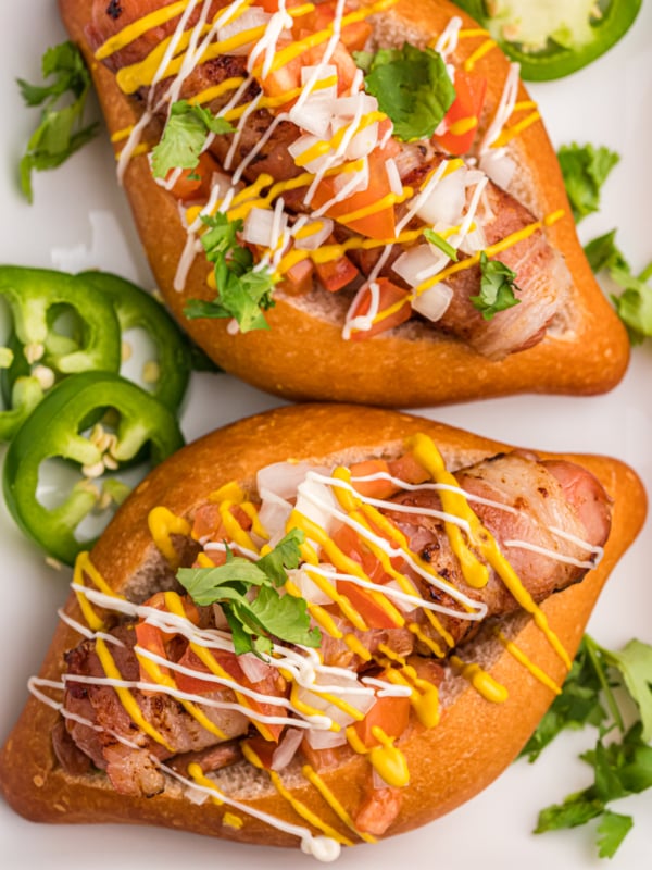 Two hot dogs are placed on a white plate with several slices of fresh jalapeno.