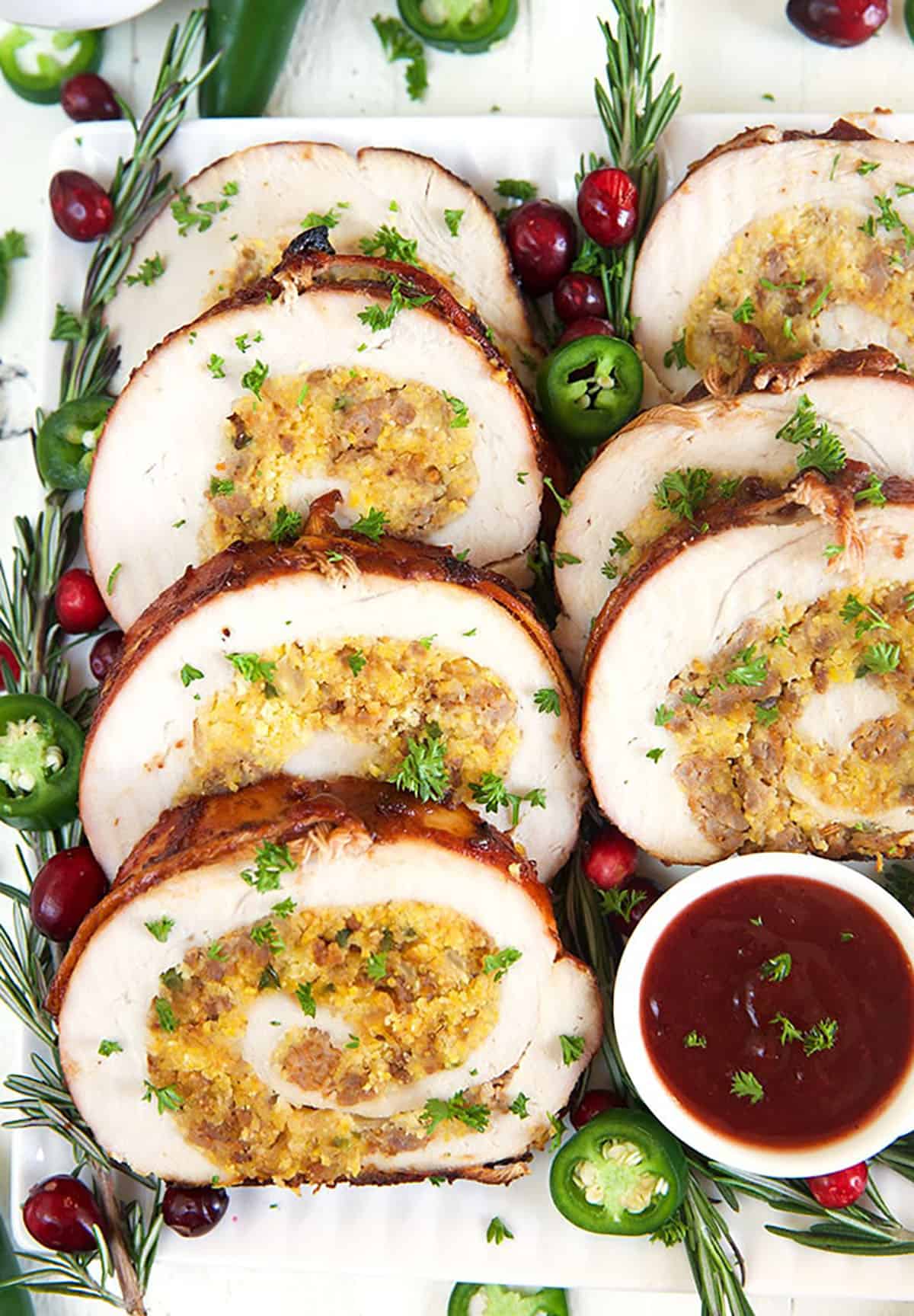 slices of turkey roulade stuffed with cornbread arranged on a platter with cranberry bbq sauce.