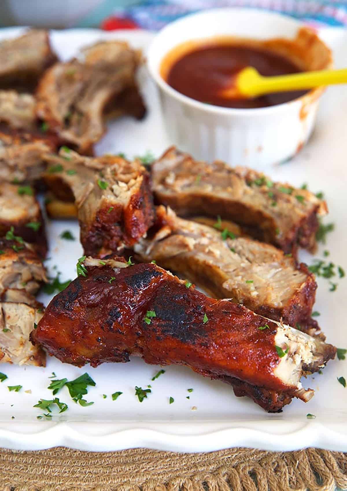 Oven Baked BBQ Ribs on a white platter with a bowl of sauce.