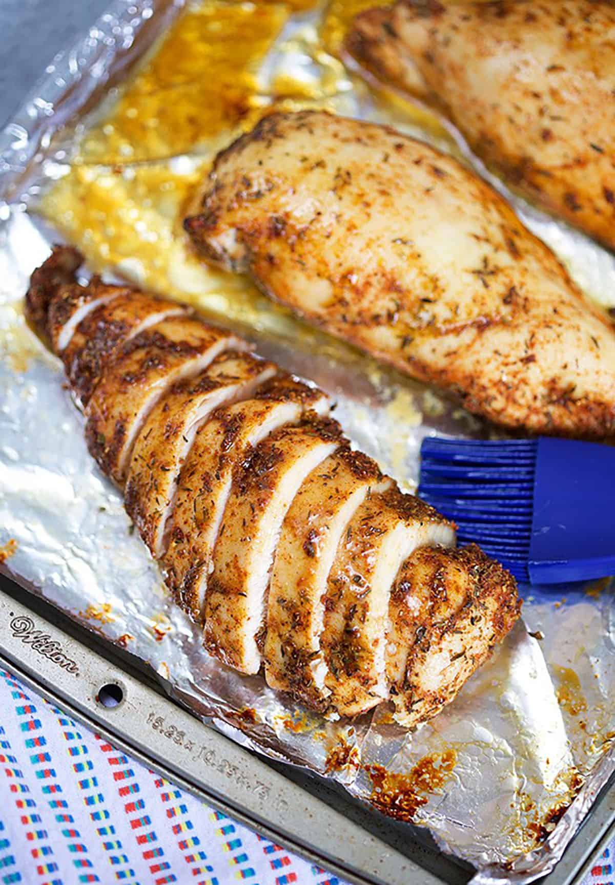 sliced baked chicken breast on a baking sheet with a blue basting brush