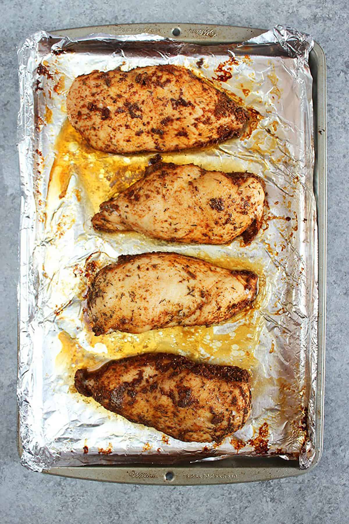 four baked chicken breasts on a baking sheet