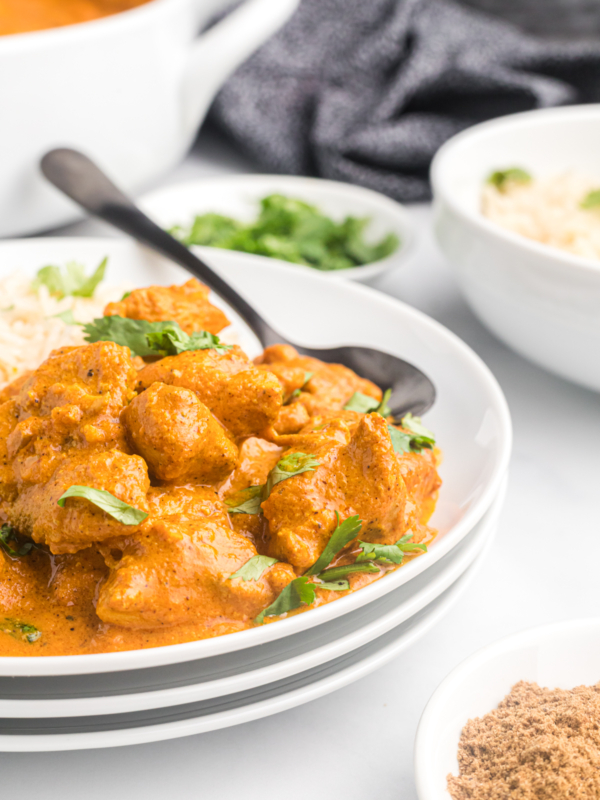 A spoon is placed on a plate with chicken tikka masala.