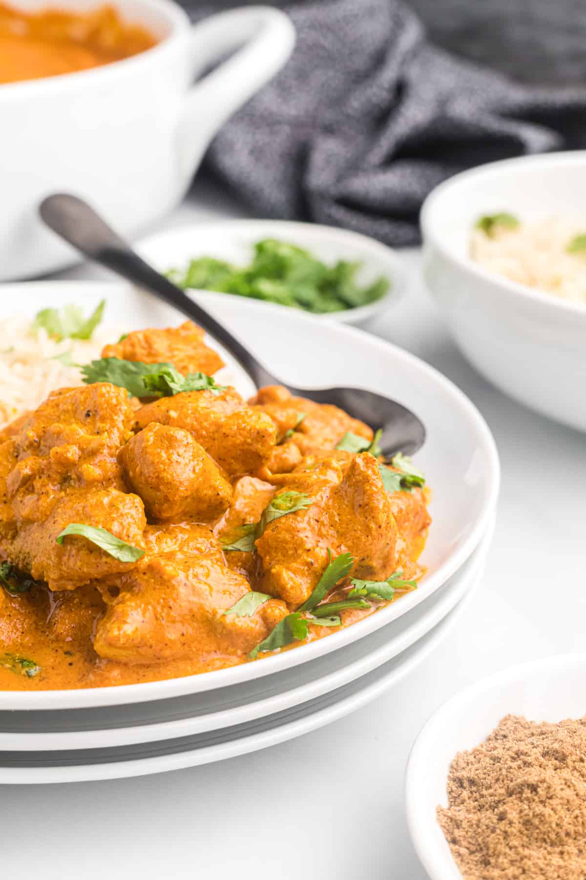 A spoon is placed on a plate with chicken tikka masala.
