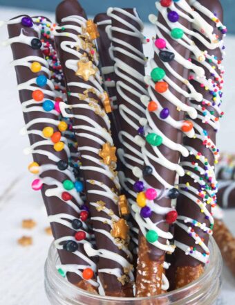 Several chocolate covered pretzel rods are placed in a glass jar.