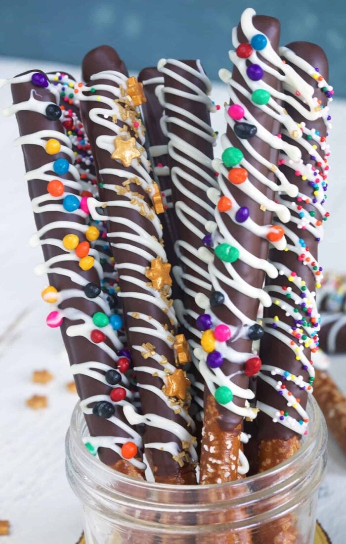 Several chocolate covered pretzel rods are placed in a glass jar.