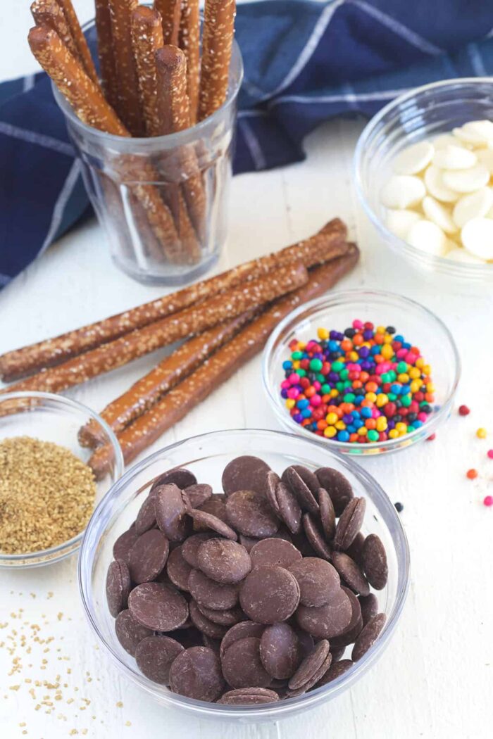 The ingredients for chocolate covered pretzel rods are placed on a white surface.