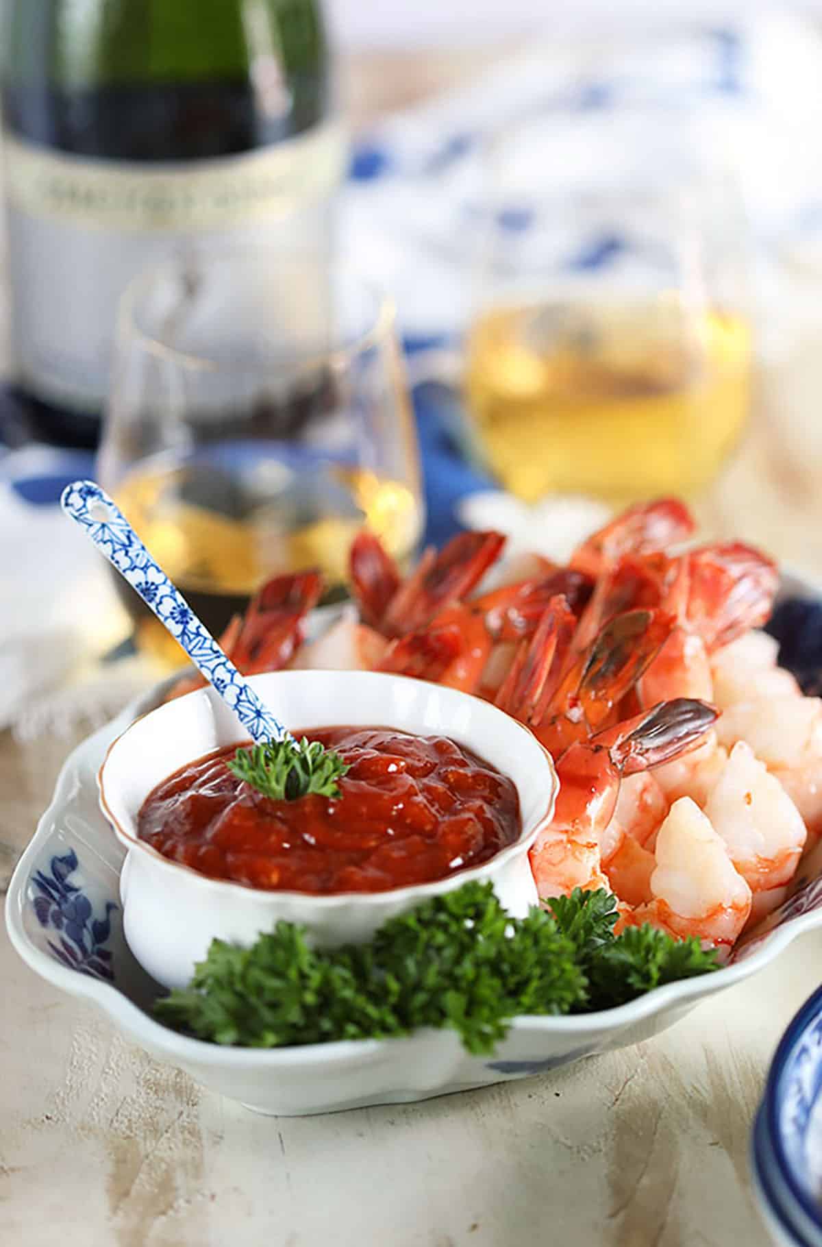 Homemade Cocktail sauce with shrimp on a blue and white plate with wine on a white background