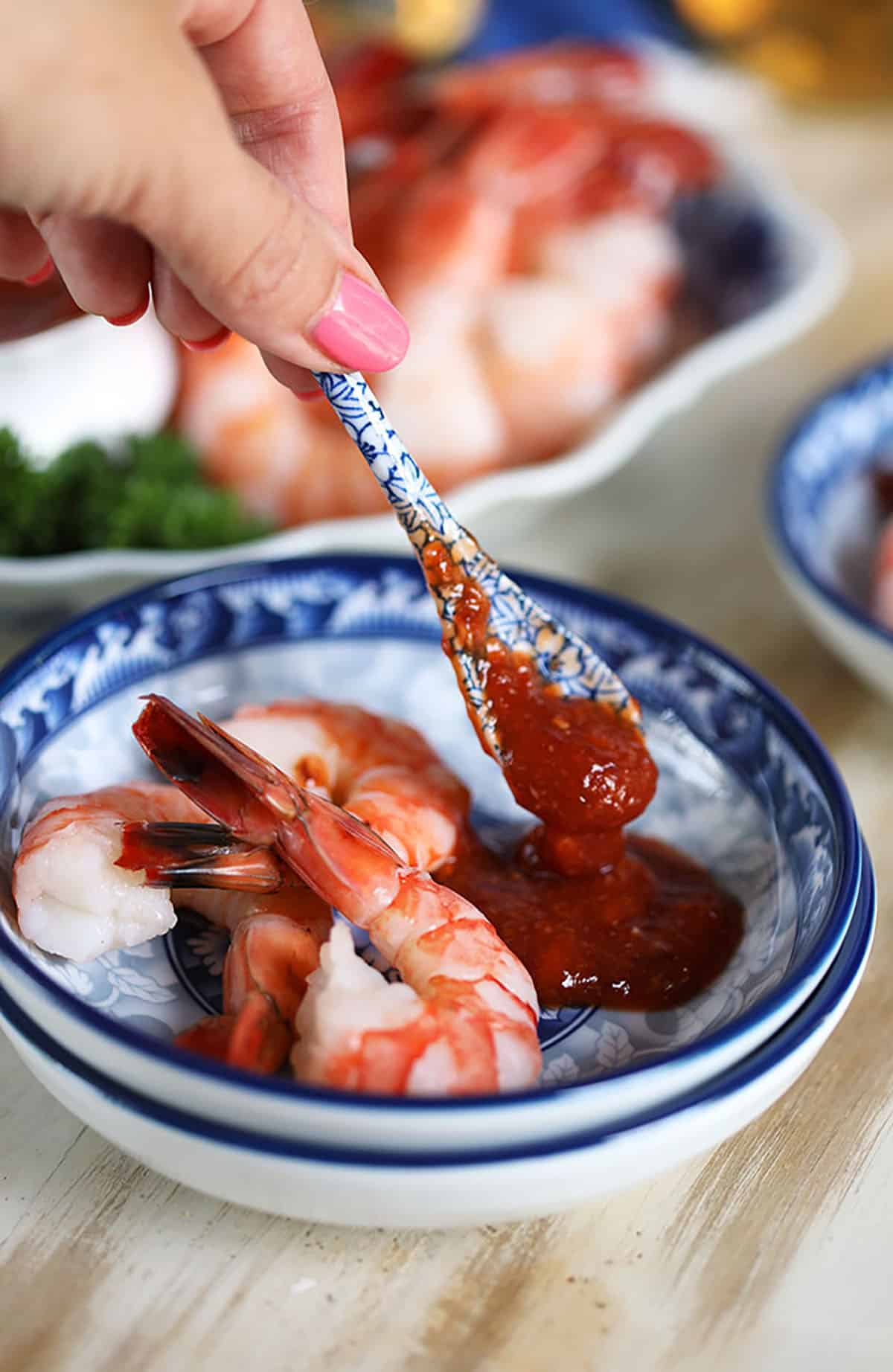 Blue and white spoon with homemade cocktail sauce and a pile of shrimp on a blue and white plate