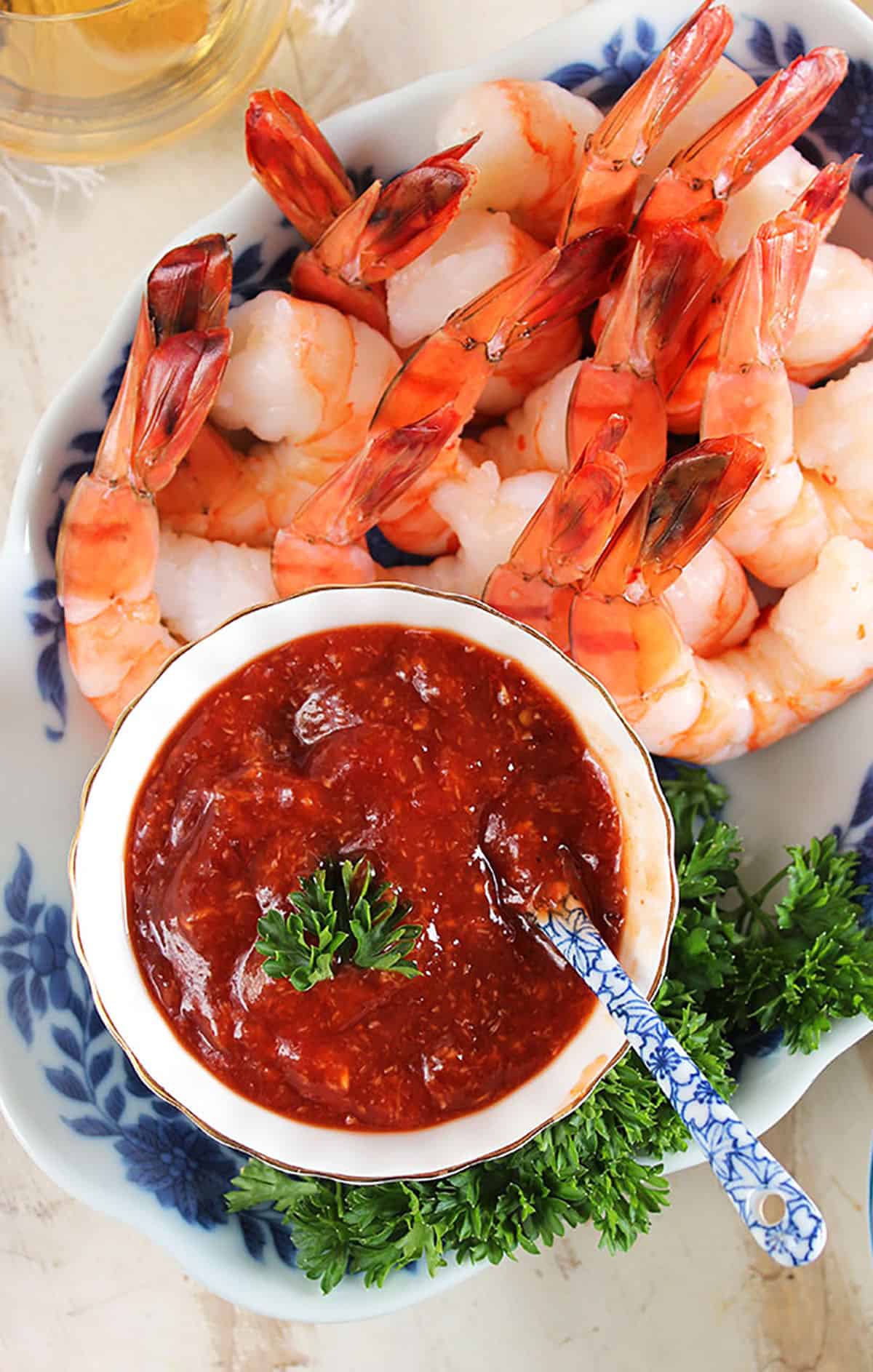 Overhead shot of homemade cocktail sauce and a pile of shrimp in a blue and white plate