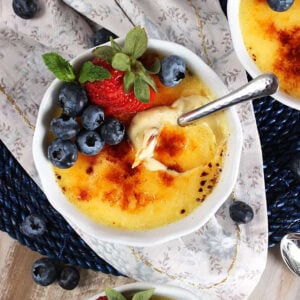 Creme Brûlée in a round white dish on a floral napkin with a spoon in it.