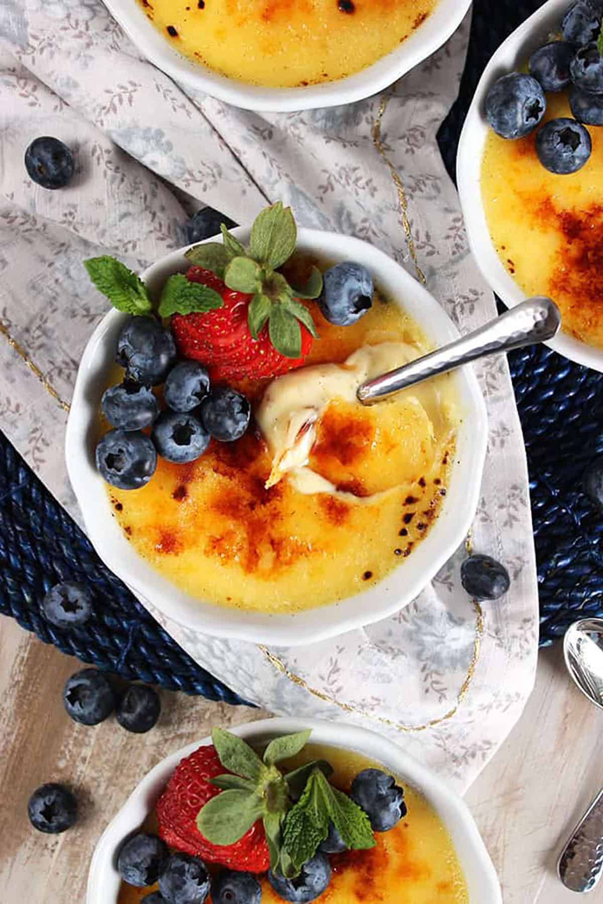 Creme Brûlée in a round white dish on a floral napkin with a spoon in it.