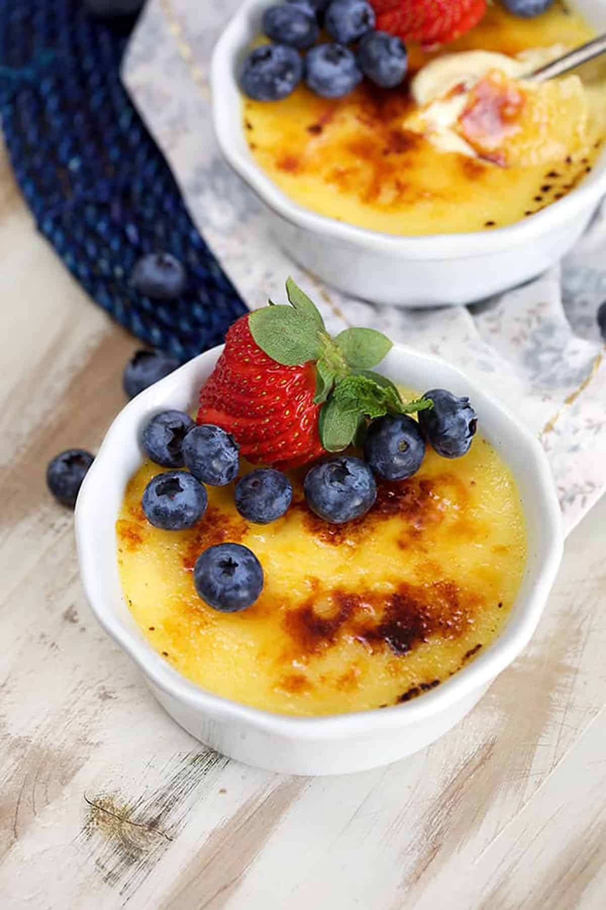 Creme brûlée in a white ramekin with blueberries and a strawberry on top.