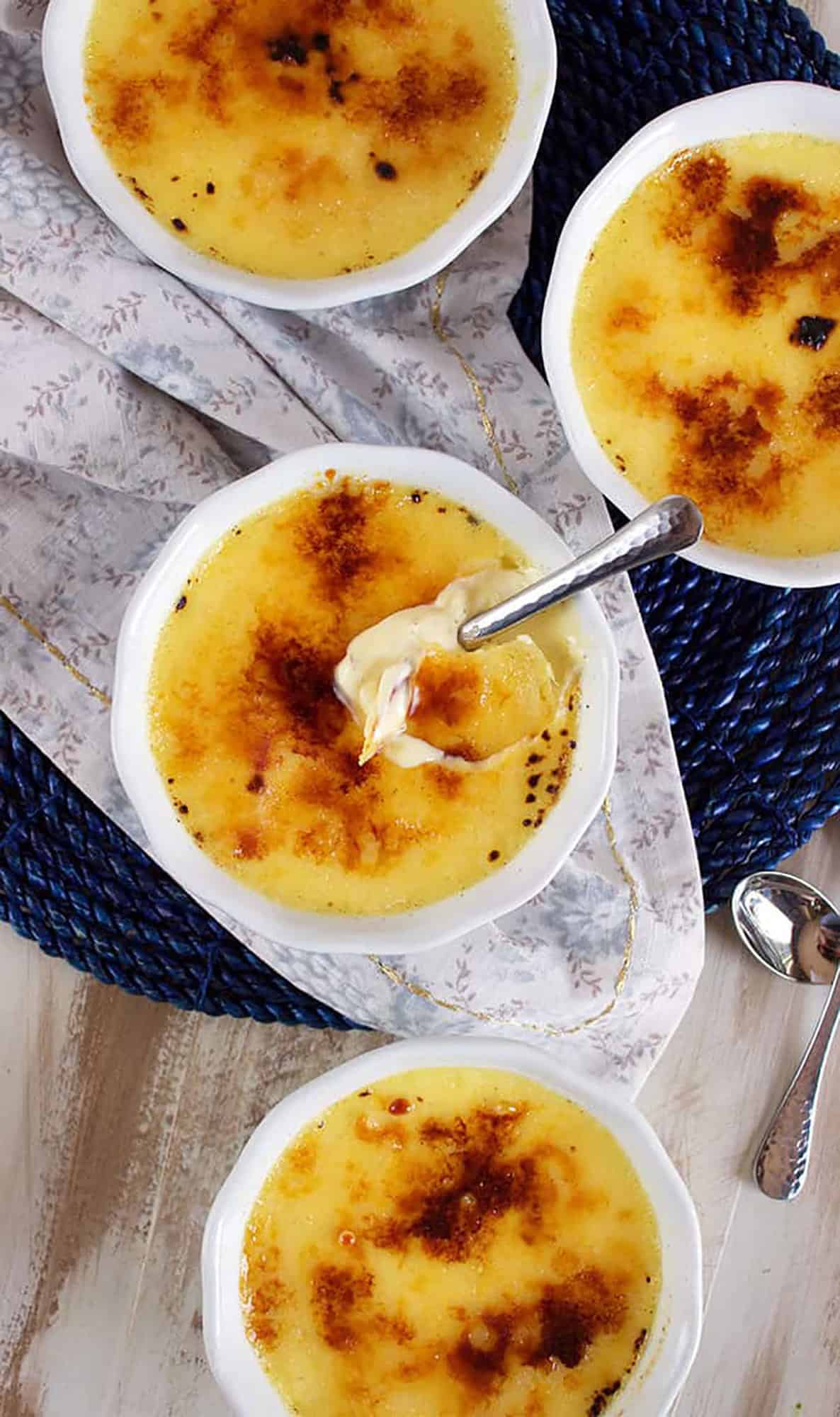 Four white round ramekins with creme brûlée in them with a silver spoon in the middle dish.