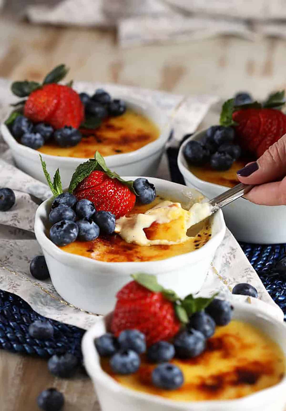 Creme Brûlée topped with berries with a spoon taking a bite out of it.