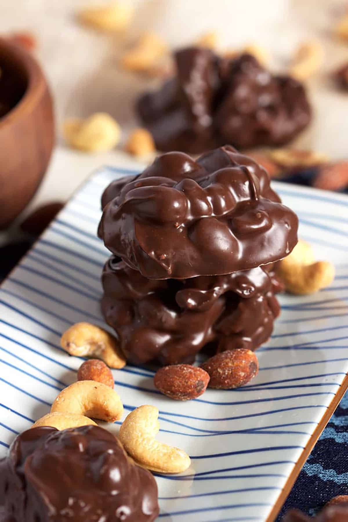 Two clusters of crockpot candy stacked on a platter with nuts around it.