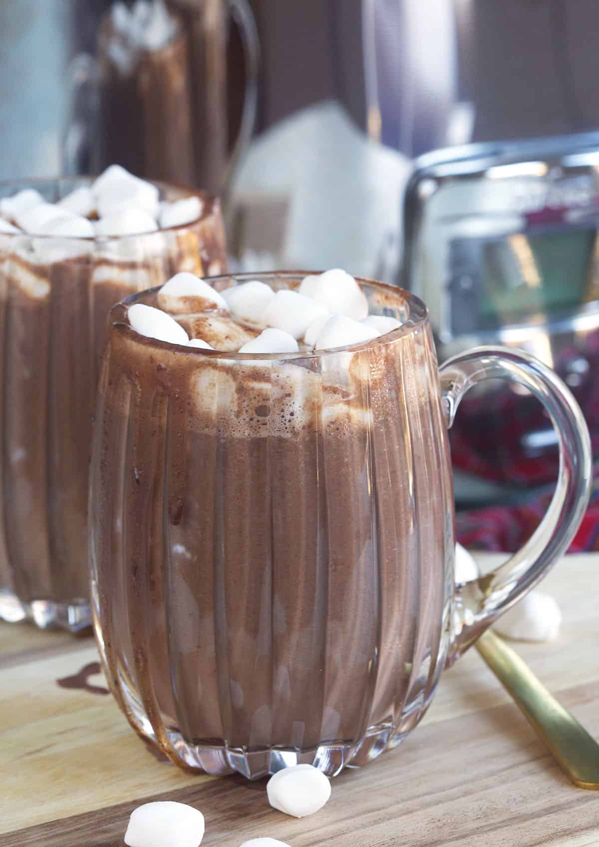 Two glasses are filled with hot chocolate and are topped with mini marshmallows. 