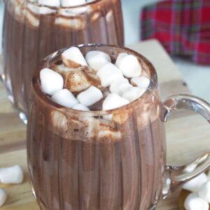 Two glass mugs filled with hot chocolate are placed on a tabletop.