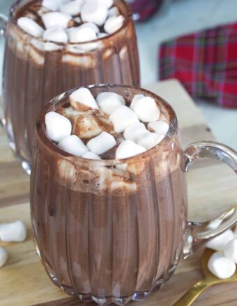 Two glass mugs filled with hot chocolate are placed on a tabletop.