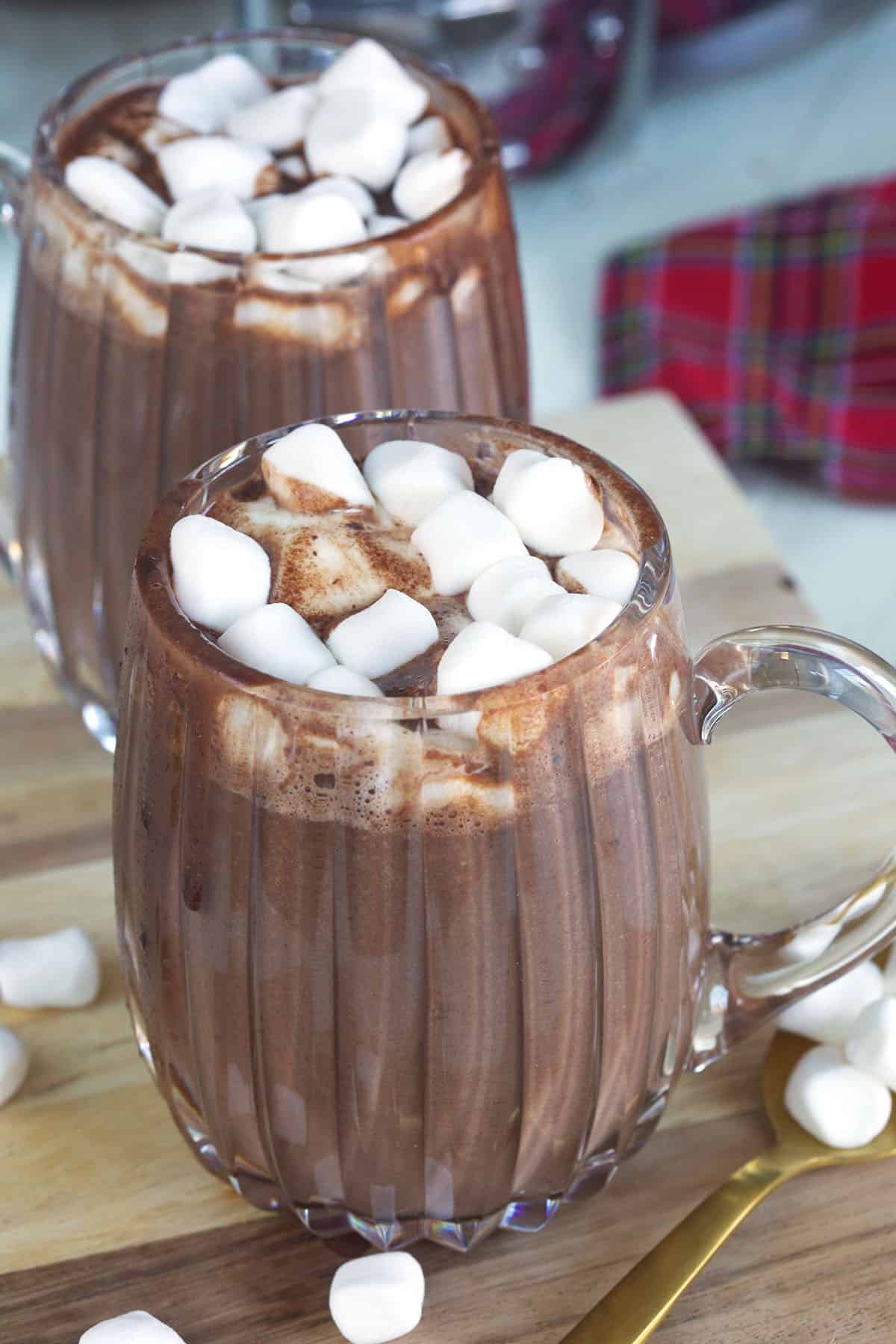 Two glass mugs filled with hot chocolate are placed on a tabletop.