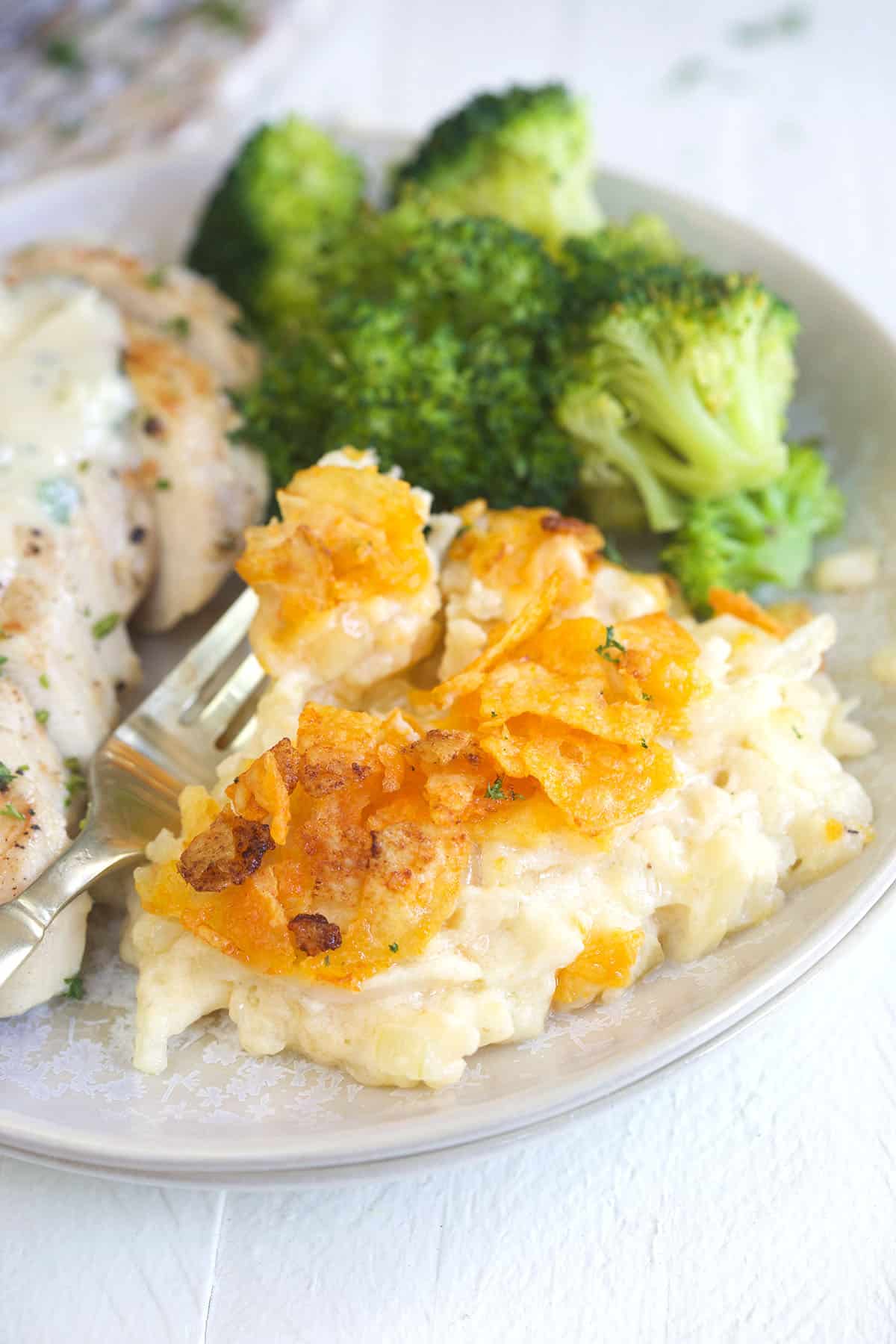 Funeral potatoes are placed next to broccoli on a plate.