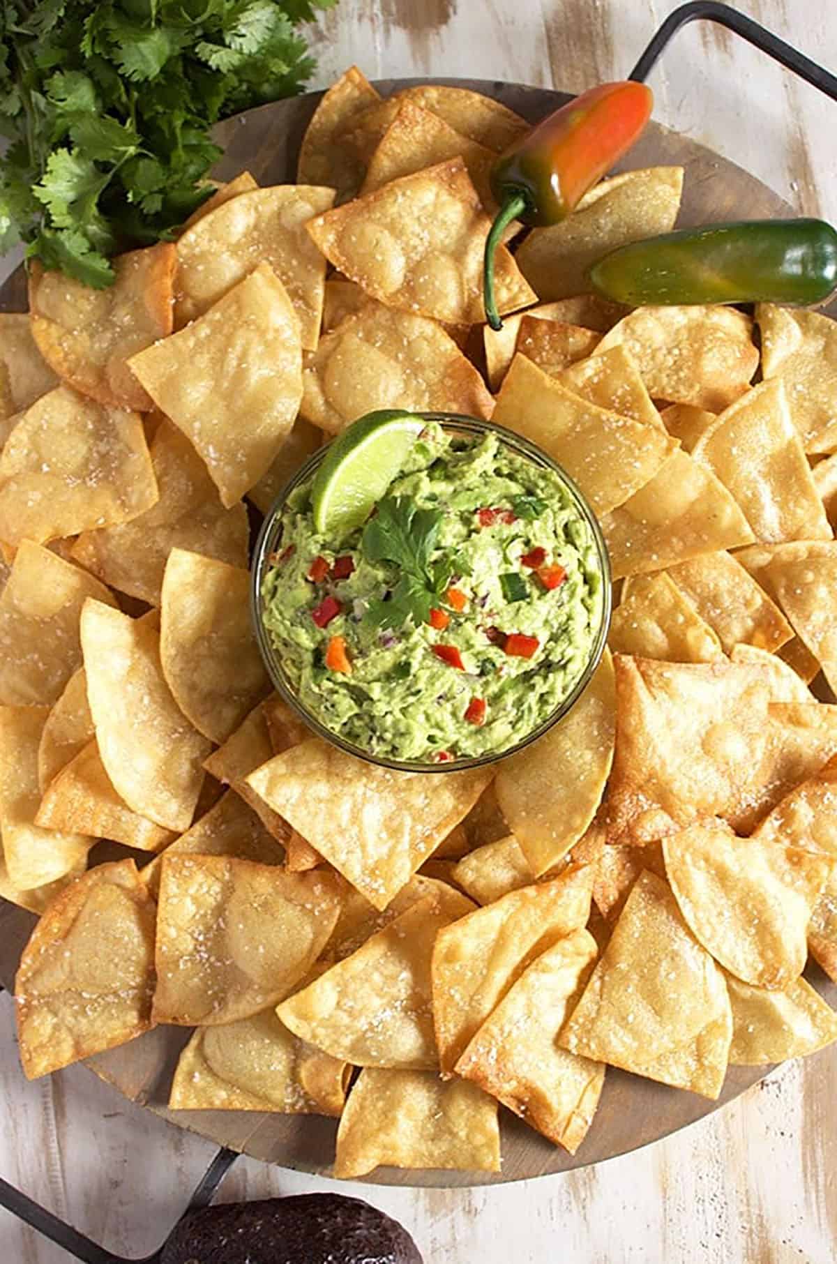 Guacamole bowl in the middle of a large tray filled with crispy tortilla chips.