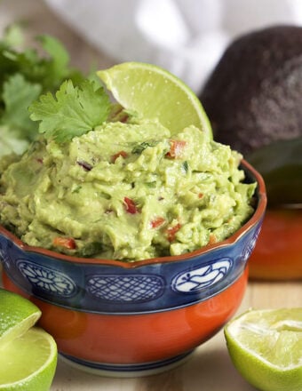 Guacamole in a red and blue bowl with a lime in it.