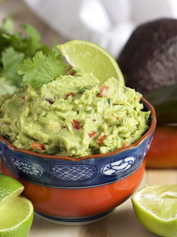 Guacamole in a red and blue bowl with a lime in it.