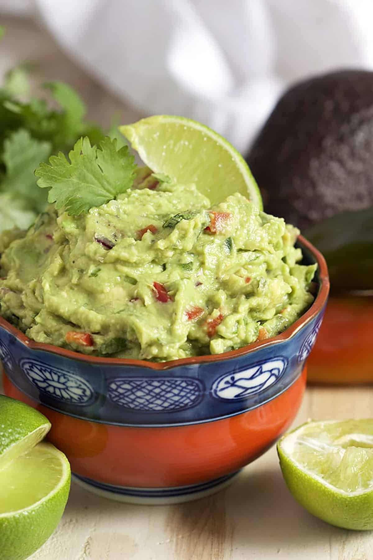 Guacamole in a red and blue bowl with a lime in it.