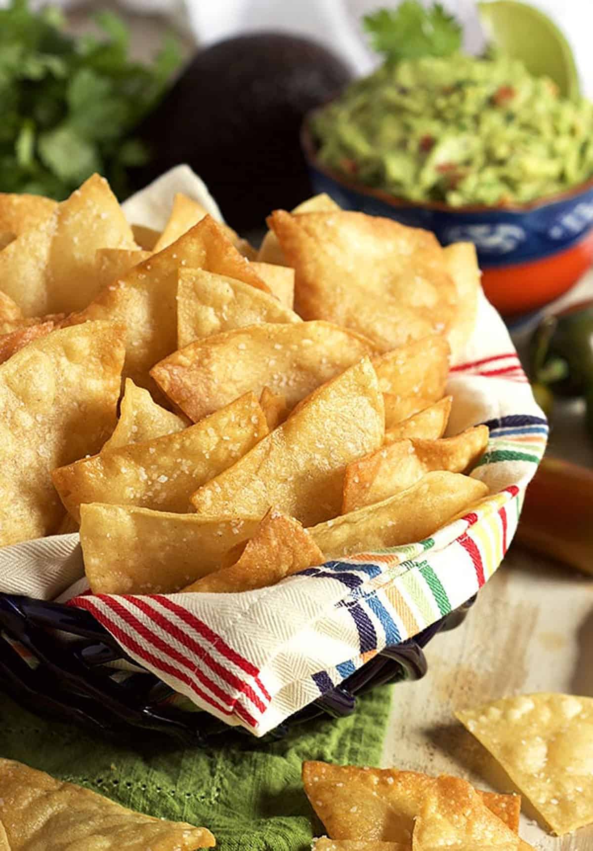 Tortilla chips in a bowl with a festive napkin and a bowl of guacamole in the background.