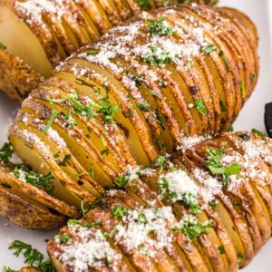 Three hasselback potatoes are garnished with cheese and fresh herbs.