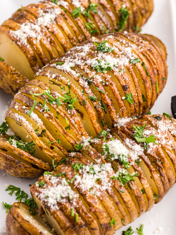 Three hasselback potatoes are garnished with cheese and fresh herbs.