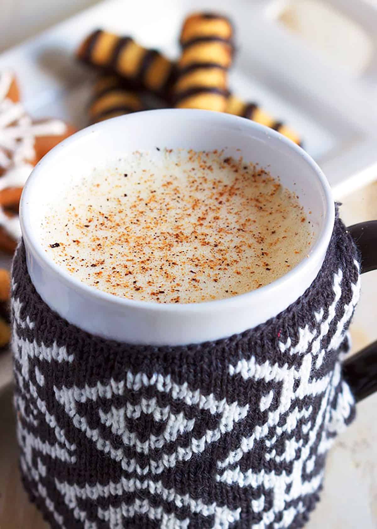 Eggnog in a white mug with a black and white sweater cozy.