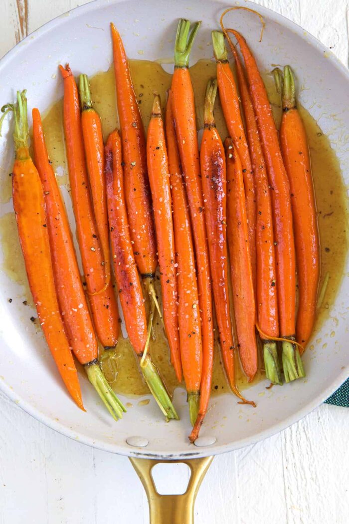 A white skillet is filled with glazed carrots.