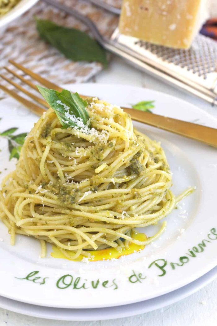 A white plate is topped with a serving of pesto pasta. 