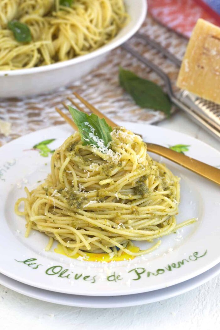 A single serving of pesto pasta is topped with a basil leaf.