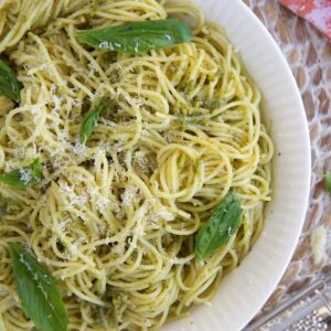 A large white bowl is filled with pasta and is topped with fresh basil leaves.