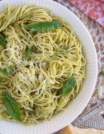 A large white bowl is filled with pasta and is topped with fresh basil leaves.