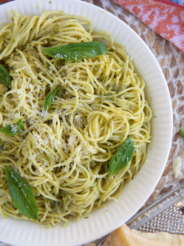 A large white bowl is filled with pasta and is topped with fresh basil leaves.