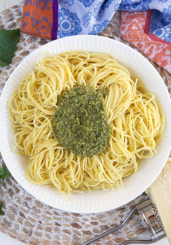 A bowl of cooked pasta is topped with a large spoonful of pesto.